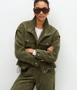 Campera Marfinno de pana verde militar, con cuello alto, cierre frontal con botones a presión, bolsillos con solapa en el pecho y cordón ajustable en el bajo.