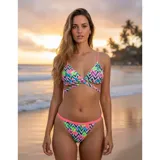 Bikini United Uy modelo Mika, compuesto por un top triangular con tiras cruzadas en la cintura y una bombacha tipo tanga. Presenta un estampado vibrante con motivos florales y geométricos en zigzag, con detalles en color rosa neón.