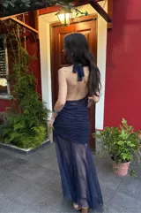 Falda larga de color azul marino confeccionada en microtul y gasa. Presenta un diseño con frunces y plisados en la zona de la cadera que brindan un ajuste al cuerpo, y una parte inferior fluida con transparencias y efecto godet.