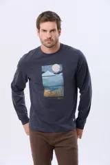 Remera de manga larga en color azul oscuro, con cuello redondo y estampado frontal de paisaje montañoso. Presenta un pequeño parche decorativo en la manga.