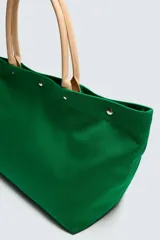 Bolso tipo shopper de tejido de algodón color verde, con asas de mano en piel color beige y cierre superior mediante botones a presión. Cuenta con compartimento principal amplio y bolsillos interiores.