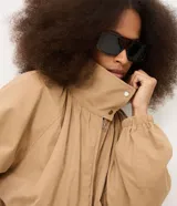 Campera bomber de sarga color beige, con diseño cortavientos, cuello alto con botones a presión y cierre frontal. Presenta mangas largas con puños elastizados, pliegues delanteros que aportan volumen y ruedo con elástico. Marca Renner.