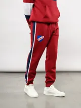 Pantalon de jogging azul de felpa, con franjas laterales en blanco y azul marino. Presenta el escudo del Club Nacional de Football en el muslo derecho y el logo de Umbro en el izquierdo.