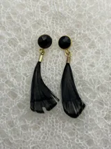 Par de aros colgantes con base redonda negra, detalles dorados y plumas negras.