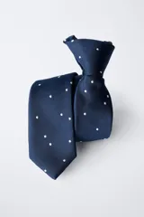 Corbata azul marino con estampado de pequeños topos blancos, cuenta con un sistema de cierre ajustable en la nuca.