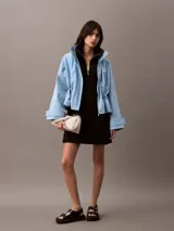 Vestido corto negro de neopreno de algodón, con cuello alto y cierre frontal de cremallera. Tiene mangas largas, corte entallado y falda con vuelo. Incluye un bordado de Calvin Klein en el pecho.