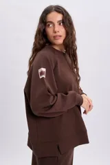 Sudadera de cuello redondo y manga larga en color marrón, con diseño holgado y detalle de etiqueta en la manga.