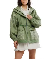 Chaqueta estilo parka o anorak de algodón color verde militar, con capucha y cordón ajustable en la cintura. Presenta parches de tela con bordados blancos de estilo paisley o floral en la parte delantera, mangas y capucha. El ruedo inferior tiene un borde festoneado con ojales.