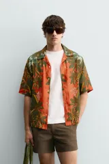Camisa de corte relajado confeccionada en tejido fluido con mezcla de viscosa y lino. Presenta cuello bowling, manga corta y cierre frontal con botones. Diseño con estampado floral en tonos verdes y naranjas.