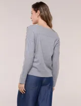 Buzo de punto fino color gris, de calce relajado, escote redondo amplio y canesú con textura acanalada. Cuenta con apliques de tachas metálicas doradas en la línea del hombro, mangas largas de hombro caído y puños y ruedo acanalados.