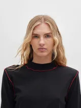 Polera de manga larga confeccionada en tela rib color bordó, con cuello alto y hombreras. Presenta costuras a la vista con pespuntes en hilo de color contrastante en el cuello, puños, hombros y ruedo.