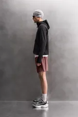 Pantalones cortos deportivos color marrón rojizo, confeccionados en tejido técnico ligero y elástico. Presentan cintura elástica ajustable con cordón interior, bolsillos frontales y un bolsillo trasero con cierre de cremallera. Los laterales tienen perforaciones para transpirabilidad y aberturas laterales en el bajo.