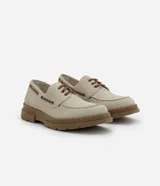 Zapato estilo dockside de color beige claro, confeccionado en gamuza sintética, con cordones marrones y suela track gruesa de goma color marrón. Presenta costuras visibles en la puntera y ojales metálicos para los cordones.