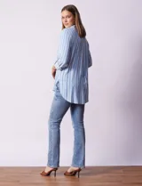 Camisa celeste con rayas verticales blancas, de corte recto y manga 3/4 regulable con presilla y botón.