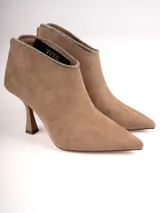 Botín color beige de gamuza con punta fina y taco de aguja. El borde superior está adornado con strass plateados.