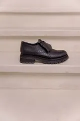Mocasín de cuero vacuno negro con textura tipo reptil, suela track de goma, cordones finos y solapa con flecos sobre el empeine.