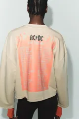 Sudadera beige de mezcla de algodón, con cuello redondo, manga larga y bajo deshilachado. Presenta un estampado frontal de la banda AC/DC con llamas naranjas y el texto "Highway to Hell" en las mangas.