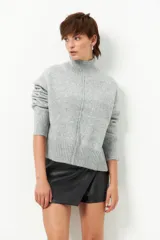 Polera de tejido de punto color gris melange, con cuello alto, manga larga con puños acanalados y costura central vertical en el frente.