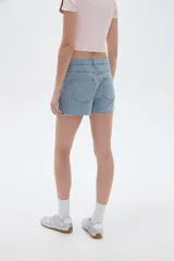 Short pollera de denim celeste claro, de tiro alto y corte mini, con diseño de falda cruzada al frente y detalle de ojales metálicos decorativos en el ruedo.