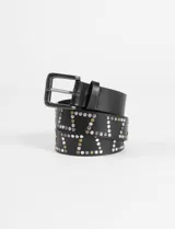 Cinturón de cuero sintético negro con hebilla metálica oscura. La correa está decorada con tachas metálicas redondas, algunas de color plateado y otras de color dorado/latón, dispuestas en un patrón que forma letras o figuras geométricas.