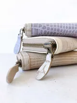 Billetera pequeña con cierre metálico, cuerpo principal de cuero lila texturizado y ribetes en color crema. Presenta un parche de cuero marrón con la palabra "chowie" escrita en cursiva.