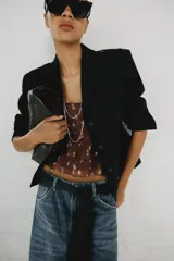 Blazer corto negro de cuello con solapa y manga larga, con hombreras, trabillas en los hombros, falsos bolsillos con solapa en el pecho y en la parte delantera, y cierre frontal con botones.