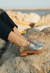 Zapato acordonado estilo oxford de cuero vacuno en color plateado metalizado, con diseño brogue, suela de goma y taco de madera.