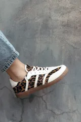 Zapatillas de estilo retro con diseño de paneles, combinando cuero beige con estampado animal print de leopardo y detalles en blanco. Presentan suela de goma color caramelo y cierre con cordones.