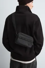 Bandolera negra de acabado engomado con compartimento principal con cierre de cremallera y bolsillo interior plano. Bolsillo frontal con cierre de cremallera. Asa de hombro ajustable y extraíble.