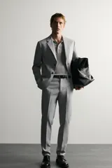 Pantalón de traje slim fit color gris, con bolsillos frontales, bolsillos traseros de doble vivo, trabillas para cinturón y cierre frontal con cremallera y botón.