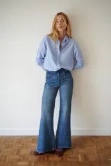 Camisa de mujer a rayas verticales blancas y rosadas, con cuello clásico, cierre de botones frontal y mangas largas con puños abotonados.