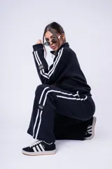 Pantalón de jogging color marrón, de corte recto y holgado, con cintura elástica y doble franja lateral blanca. Presenta una etiqueta pequeña con la marca en la parte inferior de la pierna.