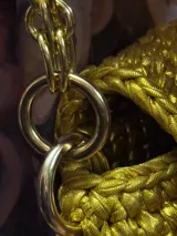 Cartera de mano tejida color dorado, con cierre metálico y cadena gruesa dorada.