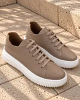 Zapatillas urbanas de cuero color tostado, con suela gruesa blanca acanalada y cordones planos al tono.