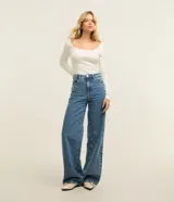 Pantalón wide leg de denim azul de talle alto con costuras pespunteadas en contraste. Cuenta con trabillas en la cintura, cierre de botón y cremallera, y bolsillos delanteros y traseros.