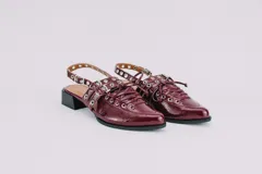 Sueco de cuero color borgoña con cordones, ojales y hebillas plateadas. Tiene tira trasera regulable con elástico.