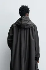 Parka de tejido con acabado engomado, diseño de corte recto y largo medio. Presenta cuello subido con capucha ajustable, cierre frontal con cremallera oculta bajo solapa con botones a presión, mangas largas y bolsillos laterales de vivo.