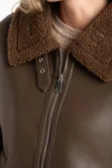 Campera tipo gamulán de cuero sintético marrón con interior y detalles de corderito en cuello, puños y ruedo. Presenta cierre frontal metálico y corte oversize.