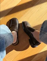 Mocasín de cuero color chocolate con acabado texturizado, diseño de punta cuadrada y suela plana con pequeño tacón.