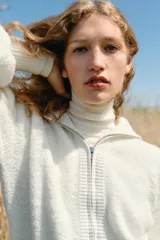 Chaqueta de punto color blanco con cuello subido, cierre frontal de cremallera metálica y mangas largas abullonadas con puños ajustados.