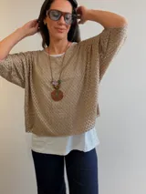 Buzo beige de tejido calado con diseño oversize, mangas tres cuartos y escote redondo, acompañado por una musculosa básica blanca interior.