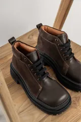 Borcegos de punta cuadrada con diseño acordonado, combinando paneles de cuero texturizado y gamuza en tonos marrones. Presentan una suela track gruesa de goma negra y cordones negros.
