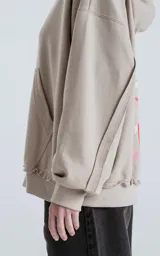 Buzo con capucha color beige claro, de calce oversize crop, con costuras expuestas en mangas y ruedo deshilachado. Presenta la palabra "AMOR" estampada en el pecho en color blanco.