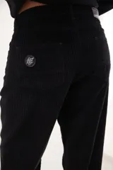 Pantalón de pana de corte ancho y tiro medio-bajo, con diseño de cinco bolsillos y acabado lavado. Presenta un aplique cuadrado decorativo en una de las piernas y un pin bordado de la marca.