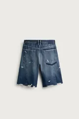 Bermuda baggy fit confeccionada en denim de algodón con lavado azul y efecto rotos en toda la prenda. Presenta diseño de cinco bolsillos, detalles de costuras en las perneras, bajo acabado irregular y cierre frontal con cremallera y botón.