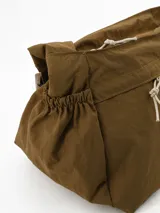 Bandolera de diseño funcional en color marrón, con cierre principal superior y dos bolsillos frontales con tiradores de cuerda. Presenta detalles fruncidos en los laterales y correa ajustable para llevar al hombro o cruzada.