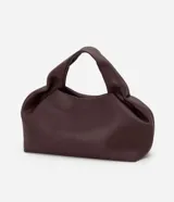 Cartera mediana de diseño estructurado en color bordó, confeccionada en poliuretano con acabado liso. Presenta asas de mano integradas con detalle fruncido, correa larga ajustable y desmontable, y cierre superior con cremallera.