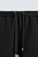 Pantalón de corte wide fit confeccionado en tejido técnico con efecto neopreno. Presenta cintura elástica ajustable con cordón, perneras anchas con costura frontal, bolsillos laterales y bolsillos traseros de plastrón.