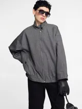 Chaqueta gris con cierre metálico, cuello alto y bolsillos laterales.