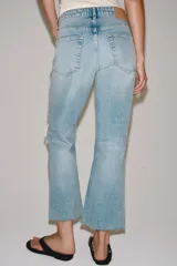 Jeans de tiro medio y corte bootcut cropped de Zara Woman Collection. Confeccionados en denim de efecto lavado en color celeste, presentan diseño de cinco bolsillos, trabillas para cinto, detalle de rotura en la rodilla izquierda y bajo evasé sin costuras. Cierre frontal con cremallera y botón metálico.